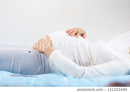 pregnant woman gently cradles her belly while lying on bed, showcasing beauty of motherhood and anticipation pregnant woman gently cradles her belly while lying on bed, showcasing beauty of motherhood and anticipation 122283489