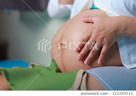 close up of pregnant woman gently touching her belly while sitting, expressing care and anticipation. image highlights beauty of pregnancy and maternal connection close up of pregnant woman gently touching her belly while sitting, expressing care and anticipation. image highlights beauty of pregnancy and maternal connection 122283513