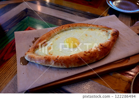 Freshly baked khachapuri served on a wooden board with a cracked egg yolk on top at a vibrant eatery Freshly baked khachapuri served on a wooden board with a cracked egg yolk on top at a vibrant eatery 122286494