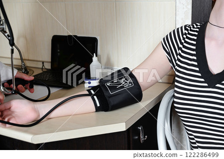 Medical professional checks blood pressure of a young woman in a clinic while wearing masks for safety during a health appointment 122286499