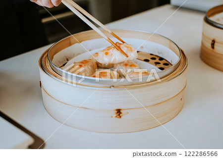 An assortment of dim sum dishes presented in bamboo steamers, with chopsticks lifting vibrant 122286566