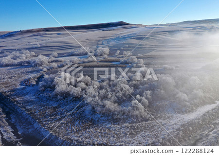 Aerial view of snow-covered landscape with fog rolling over fields and hills in winter season 122288124