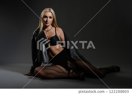 Stylish model in lingerie poses confidently with leather jacket in studio Stylish model in lingerie poses confidently with leather jacket in studio 122288603