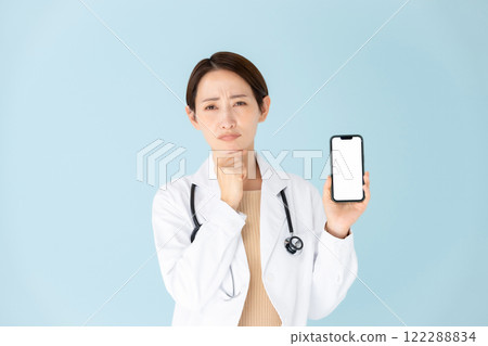 Woman in white coat, stethoscope, smartphone, worries 122288834