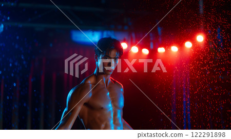 Asian male ballet dancer performing under dramatic lighting and rain in an urban setting during a nighttime event 122291898