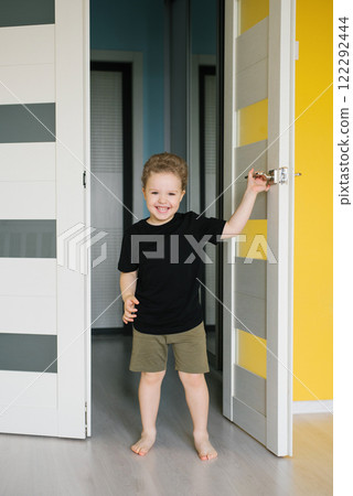 Happy smiling child boy stands in front of door. Playful and cheerful atmosphere Happy smiling child boy stands in front of door. Playful and cheerful atmosphere 122292444