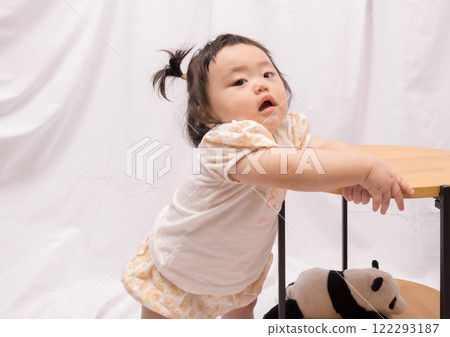 [Baby with twin tails standing up holding onto a table] 122293187