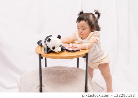 [Pigtailed baby standing on a table with smartphone] 122293188
