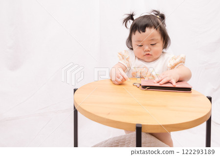 [Pigtailed baby standing on a table with smartphone] 122293189