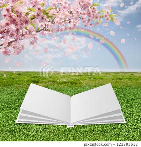 An open white book stands out against a green field with falling cherry blossoms and a blue sky with a rainbow 122293618