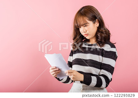 Portrait of beautiful Asian young woman sad tired strain holding paper calculating bills on hand, female person problem she hold worried over bill, studio shot isolated on pink background Portrait of beautiful Asian young woman sad tired strain holding paper calculating bills on hand, female person problem she hold worried over bill, studio shot isolated on pink background 122293829