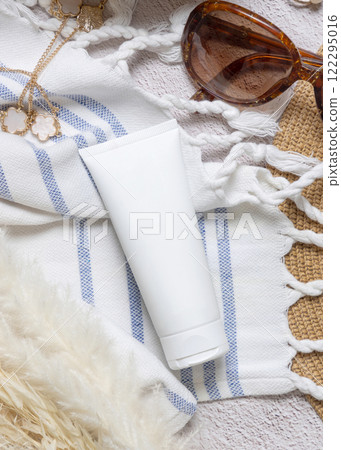 Sunscreen cream tube on towel near hat, dryed grass and sunglasses closeup, cosmetic mockup Sunscreen cream tube on towel near hat, dryed grass and sunglasses closeup, cosmetic mockup 122295016