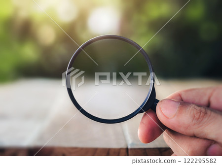 Hand holding magnifying glass on natural background. man looking through magnifying glass, searching or investigating something. Find keywords concept. closeup. 122295582