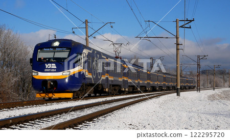 A passenger train travels on a snow-covered railway on a clear winter day. A passenger train travels on a snow-covered railway on a clear winter day. 122295720