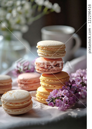 Colorful macarons arranged on a table with fresh flowers and a cup in a cozy kitchen setting during daylight. 122296416