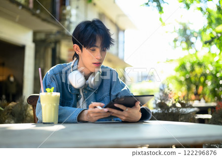 Young stylish man sitting at cafe table with a refreshing beverage and using digital tablet 122296876