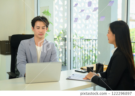 Asian male employe reviewing information on his laptop and evaluates candidate during an interview 122296897