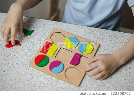 Close-up of hands of unrecognizable child inserting wooden blocks into the grooves of the educational toy. Concept of children education. Close-up of hands of unrecognizable child inserting wooden blocks into the grooves of the educational toy. Concept of children education. 122298762