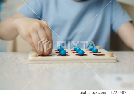 Close-up of the hands of an unrecognizable child playing a game for the development of memory and thinking. Wooden ecological toys. The concept of children's education. 122298763