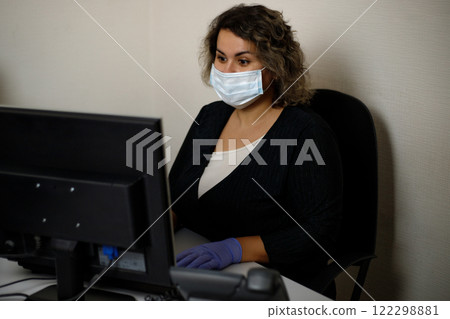 A call center agent working on the support hotline in the office, wearing a mask and gloves. The call center operator is talking to the customer. Close-up. A call center agent working on the support hotline in the office, wearing a mask and gloves. The call center operator is talking to the customer. Close-up. 122298881