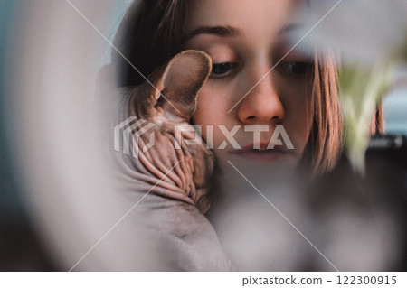 A young woman hugs a bald Canadian Sphynx cat. Creative photo of a human with lovable hairless feline domestic animal, pet. Sphinx kitty portrait. 122300915