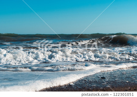 Beautiful blue sea and large calm waves and foam. Wave splashing over pebbles at sea. Rolling ocean waves. Summer paradise beach background. Powerful sea waves Beautiful blue sea and large calm waves and foam. Wave splashing over pebbles at sea. Rolling ocean waves. Summer paradise beach background. Powerful sea waves 122301051