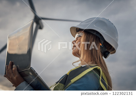 A skilled female engineer uses her laptop to oversee complex wind turbine operations, showcasing her expertise and promoting innovation and sustainability in technology aligned with nature 122302131
