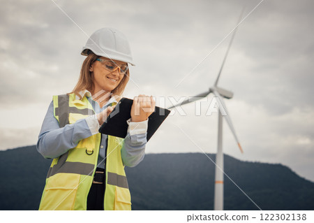 A skilled female engineer is meticulously inspecting the efficiency of a wind turbine while utilizing a digital tablet in the diverse and rapidly advancing field of renewable energy solutions 122302138