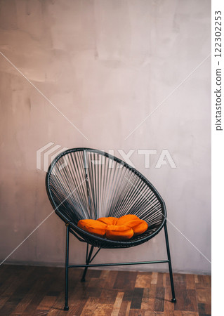 black artificial rattan chair with orange pillow against grey wall. photo zone with chair black artificial rattan chair with orange pillow against grey wall. photo zone with chair 122302253