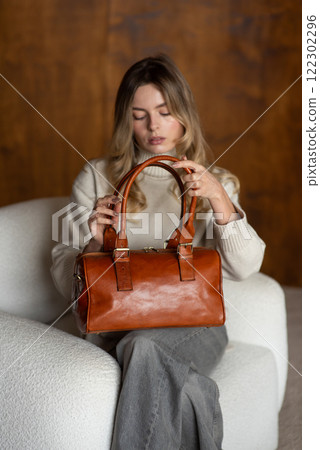 beautiful girl in gray pants and beige sweater posing with a small shiny brown leather bag beautiful girl in gray pants and beige sweater posing with a small shiny brown leather bag 122302296