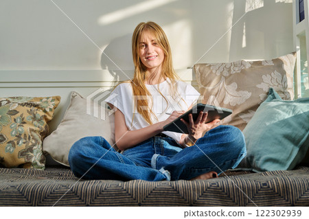 Portrait of female student on couch with digital tablet, studying at home 122302939