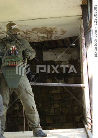 A tactical operator dressed in military gear and a cap stands inside an abandoned building, holding a rifle. 122303095