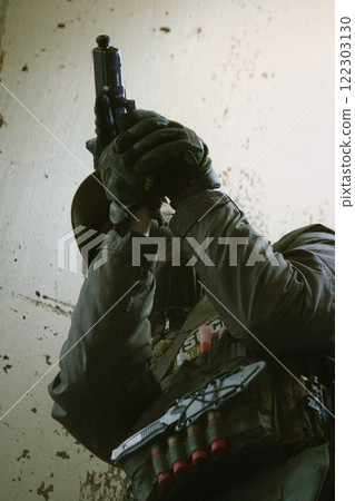 A tactical operator in military gear ascends a staircase in a dimly lit, abandoned building, aiming a rifle upwards. 122303130