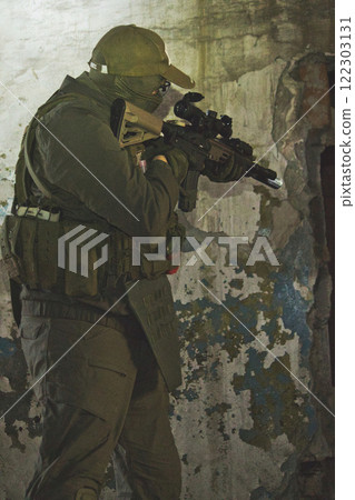 A tactical operator in military gear ascends a staircase in a dimly lit, abandoned building, aiming a rifle upwards. 122303131
