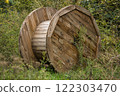 Two large wooden cable reels lie abandoned in an overgrown field surrounded by tall grass and wild vegetation.  122303470