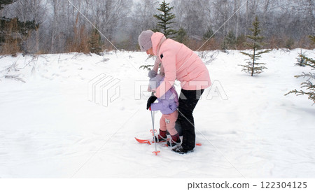 In a snowy landscape, a young mother supports her daughter on her first skiing experience, embracing seasonal winter sports and family activities In a snowy landscape, a young mother supports her daughter on her first skiing experience, embracing seasonal winter sports and family activities 122304125