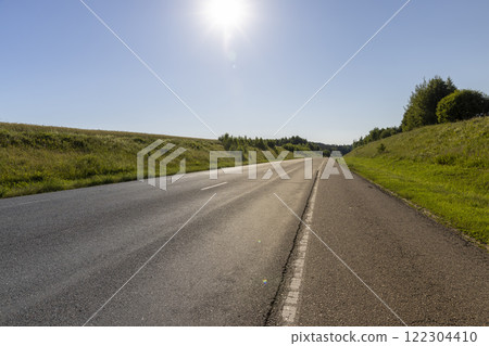 an empty straight paved road against a blue sky background 122304410