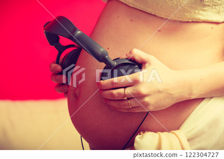 Woman with headphones on pregnant belly Woman with headphones on pregnant belly 122304727