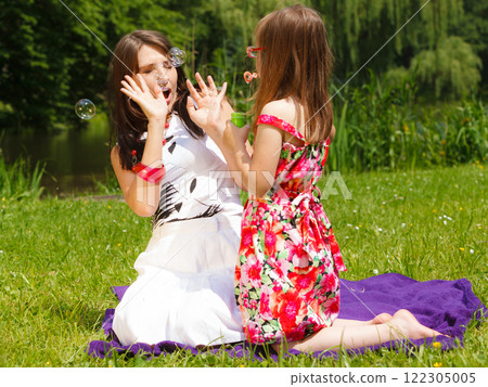 Mother and little girl blowing soap bubbles in park. Mother and little girl blowing soap bubbles in park. 122305005