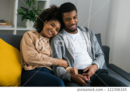 African American couple wife husband watching movie. Family pastime and leisure, watch television, rest. Relaxed man and woman watching TV series together sitting on couch at home enjoying eating African American couple wife husband watching movie. Family pastime and leisure, watch television, rest. Relaxed man and woman watching TV series together sitting on couch at home enjoying eating 122306165