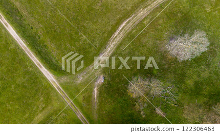 Aerial view of a grassy landscape with intersecting dirt paths, surrounded by scattered trees and open green fields, capturing a tranquil and natural outdoor scene. Aerial view of a grassy landscape with intersecting dirt paths, surrounded by scattered trees and open green fields, capturing a tranquil and natural outdoor scene. 122306463