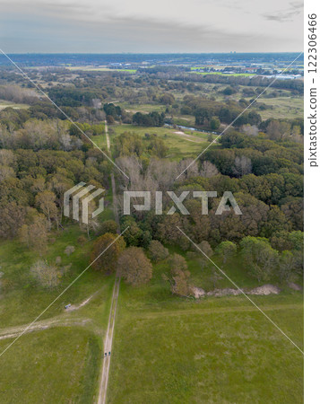 Aerial view of a serene landscape featuring green fields, a dirt road, and a mix of dense and sparse trees, with an open horizon under a calm, clear sky. 122306466