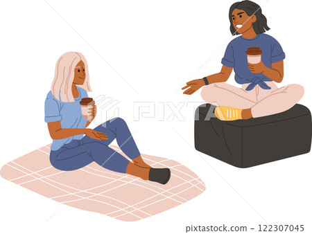 Two diverse young female friends holding disposable coffee cups talking and smiling while sitting on a blanket and a pouf, enjoying their free time, isolated on white background 122307045