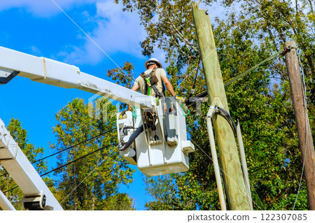 Technician handles wiring on power pole using lift, set against home Technician handles wiring on power pole using lift, set against home 122307085