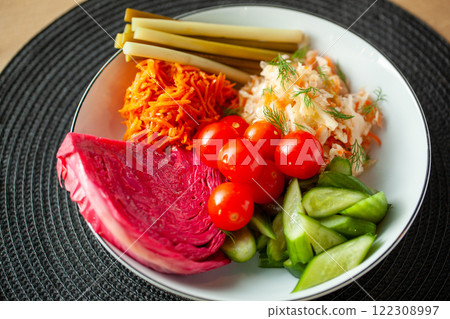 Traditional Russian pickled vegetables including cabbage carrots cherry tomatoes and cucumbers arranged on a white plate 122308997