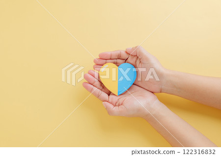 Yellow background with hands holding a divided yellow-blue heart marks Down Syndrome Day. Supporting Autism 122316832