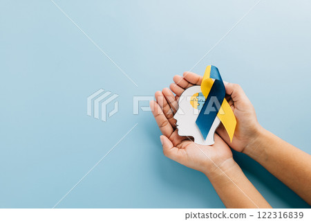 Hands holding a head with puzzle pieces and a ribbon. Celebrating Down Syndrome Day 122316839