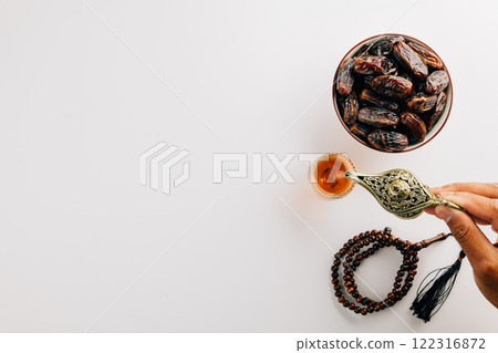 Hand pouring tea from a teapot with dates and prayer beads on white. Ramadan celebration Hand pouring tea from a teapot with dates and prayer beads on white. Ramadan celebration 122316872