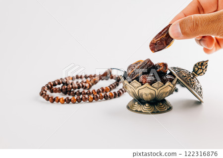Holy Ramadan celebration with hands arranging dates and beads in ornate dish 122316876