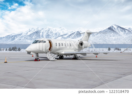 Modern white executive jet plane with an opened gangway door at the winter airport apron on the background of high scenic snow capped mountains Modern white executive jet plane with an opened gangway door at the winter airport apron on the background of high scenic snow capped mountains 122318470
